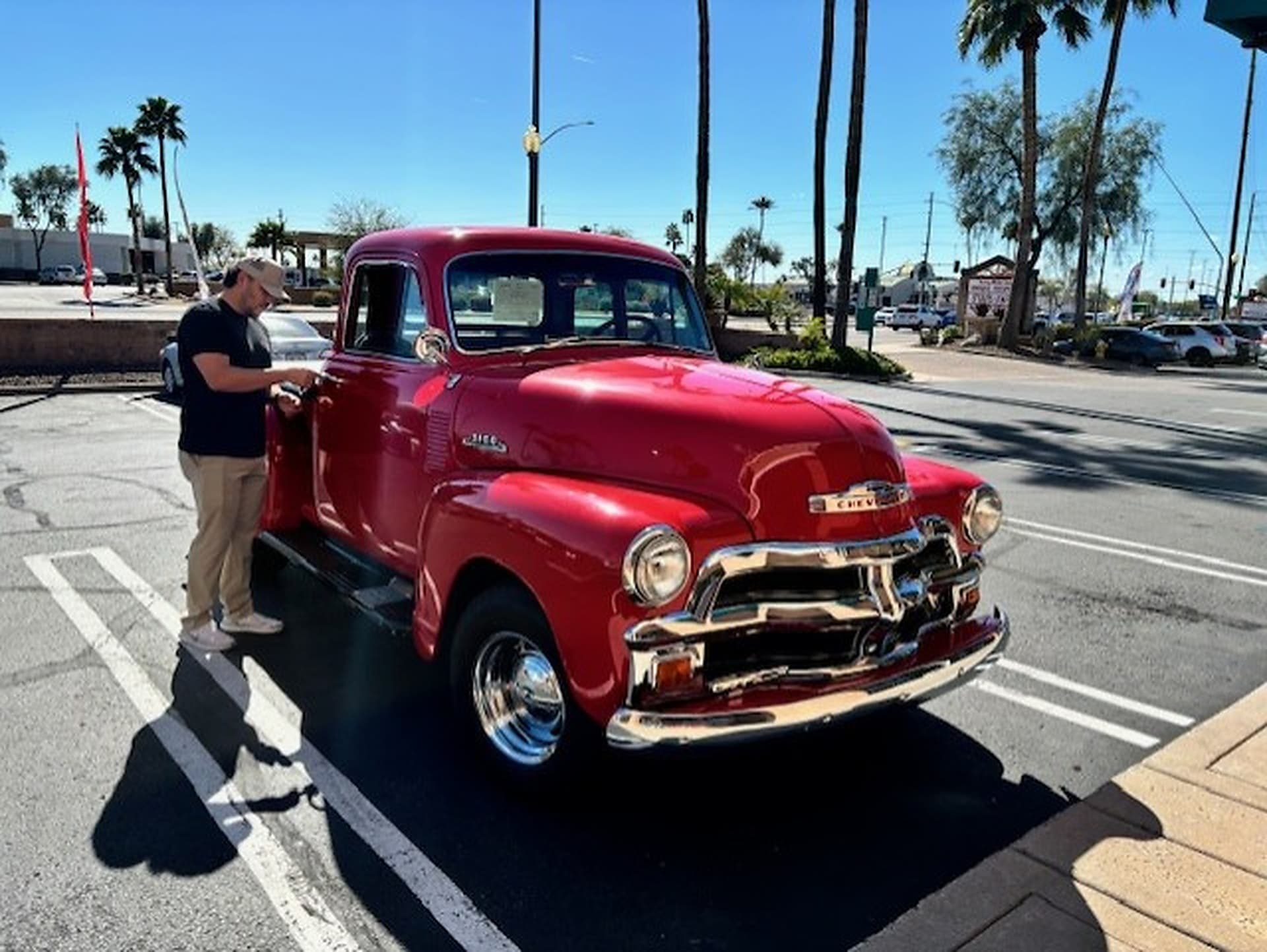 Locksmith working at the driver door of a red classic pickup truck in a Mesa parking lot