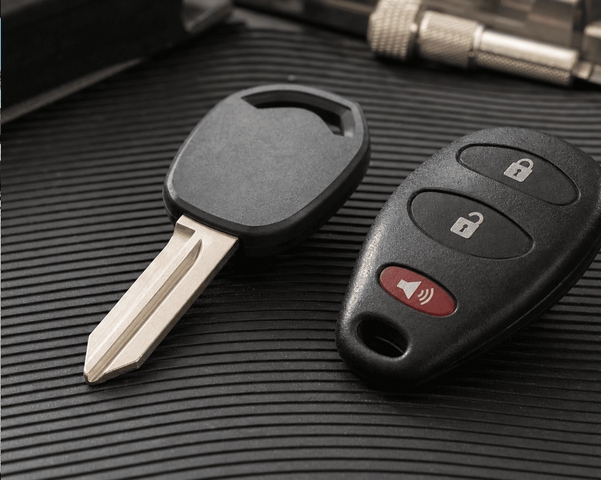 A transponder car key and a three-button remote fob on a ribbed workshop mat