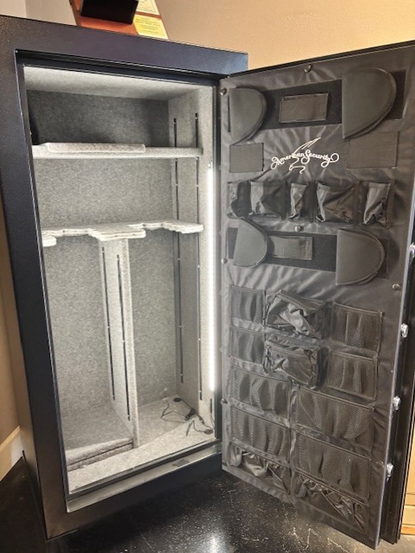 Open gun safe with a gray fabric interior, shelving and a door organizer