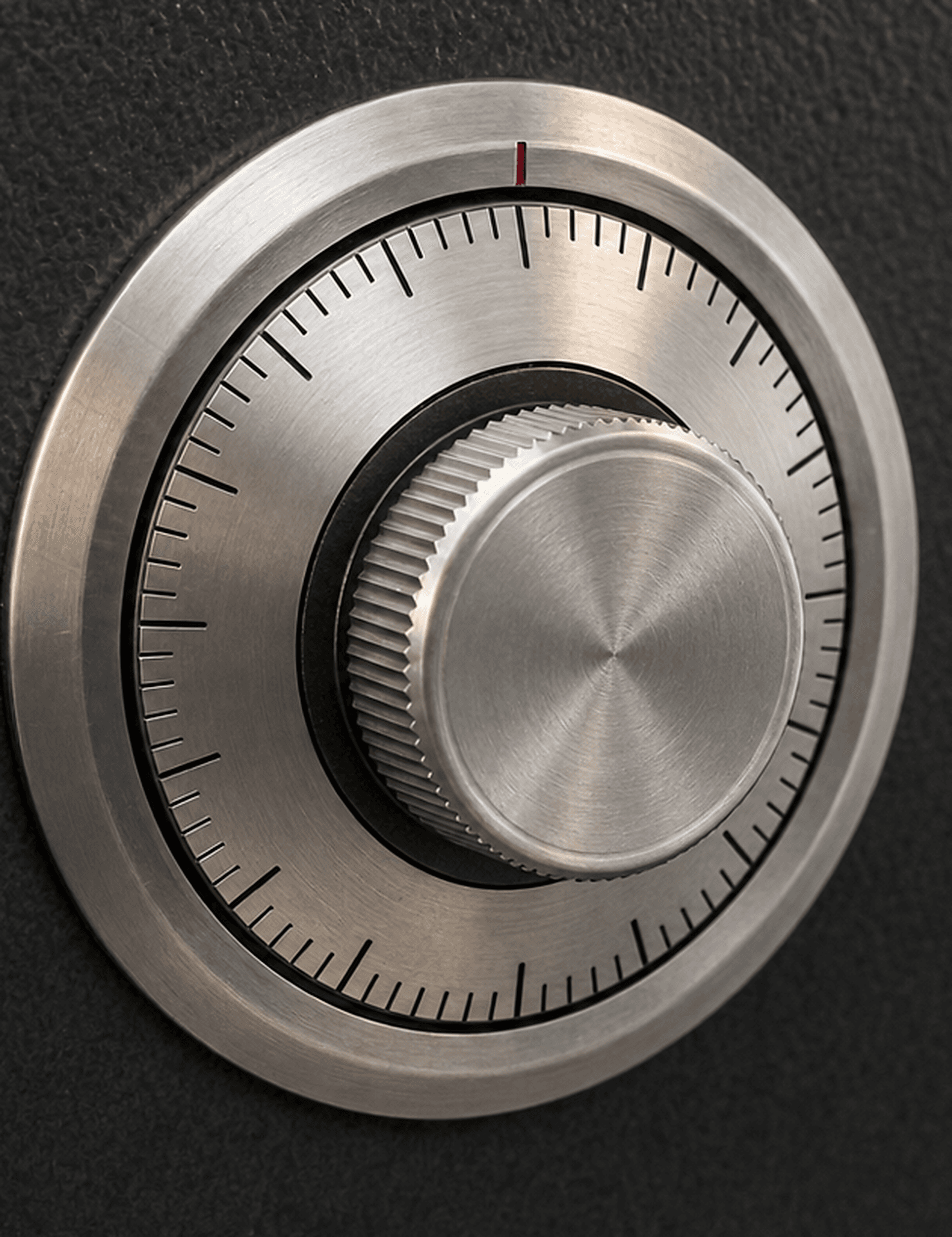 Brushed steel combination dial with a red index mark on a black safe door